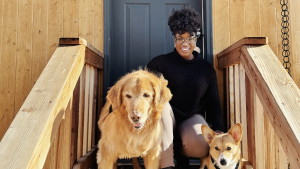 A vibrant dog park bathed in sunlight features abundant greenery with mature trees, offering ample shade for leisurely outdoor activities. In the distance is a well-equipped playground that presents an additional activity area. An inviting picnic table spreads out nearby, ideal for enjoying meals al fresco or taking relaxing breaks from play. A neatly-placed trash bin aids in maintaining the park's cleanliness for everyone's enjoyment. Dominating the scene is a generously wide dirt path gracefully curving through the expanse of grass, promising exploratory walks and lively fetch games.